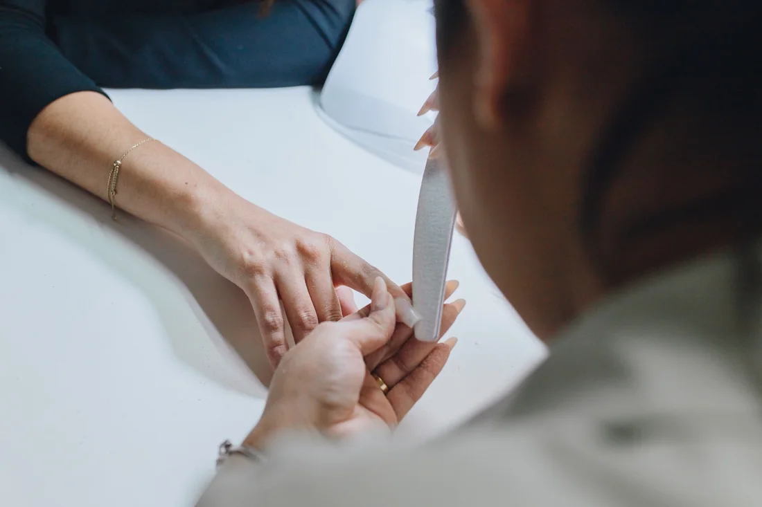 A nail professional filing a client's nails during a manicure